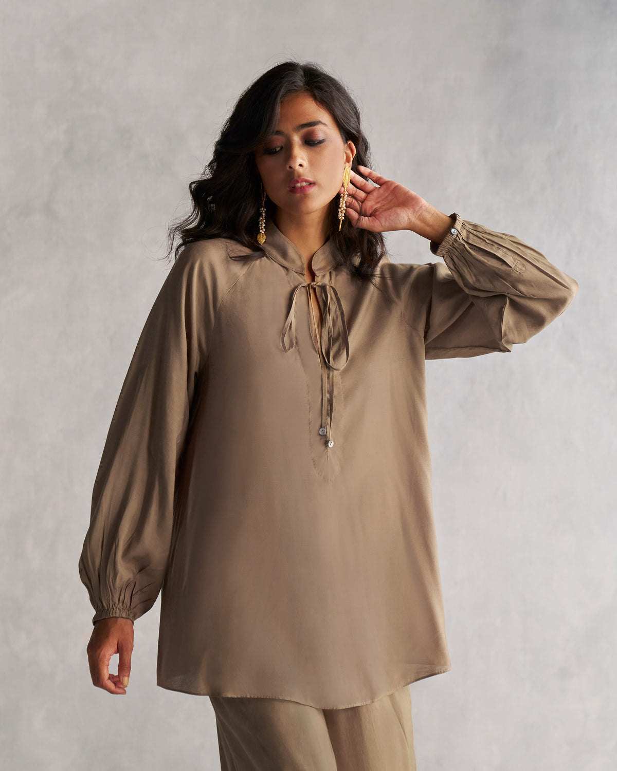 Person wearing an oak brown raglan blouse with collar ties.