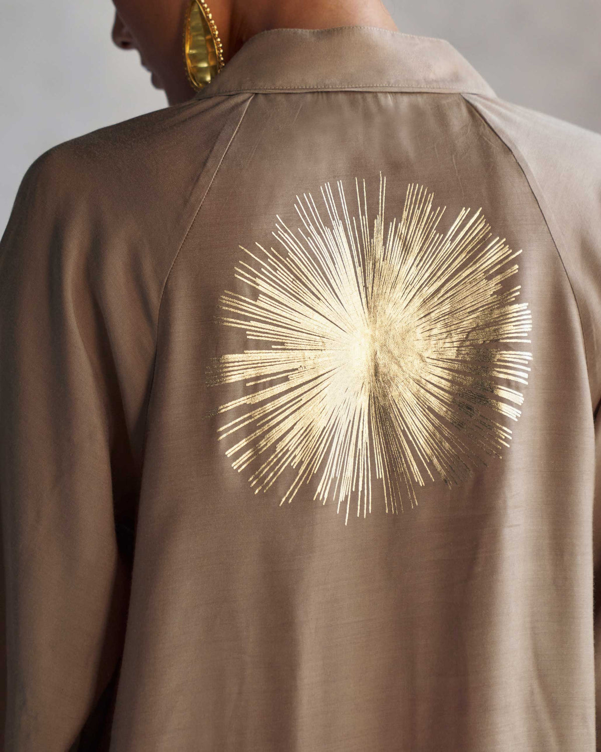 Close-up of a gold sunburst print on the back of an oak brown raglan blouse.