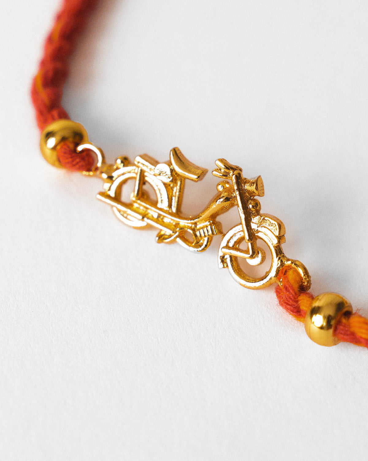 Close-up of Motor Cycle Rakhi showing a gold motorcycle charm on red thread.