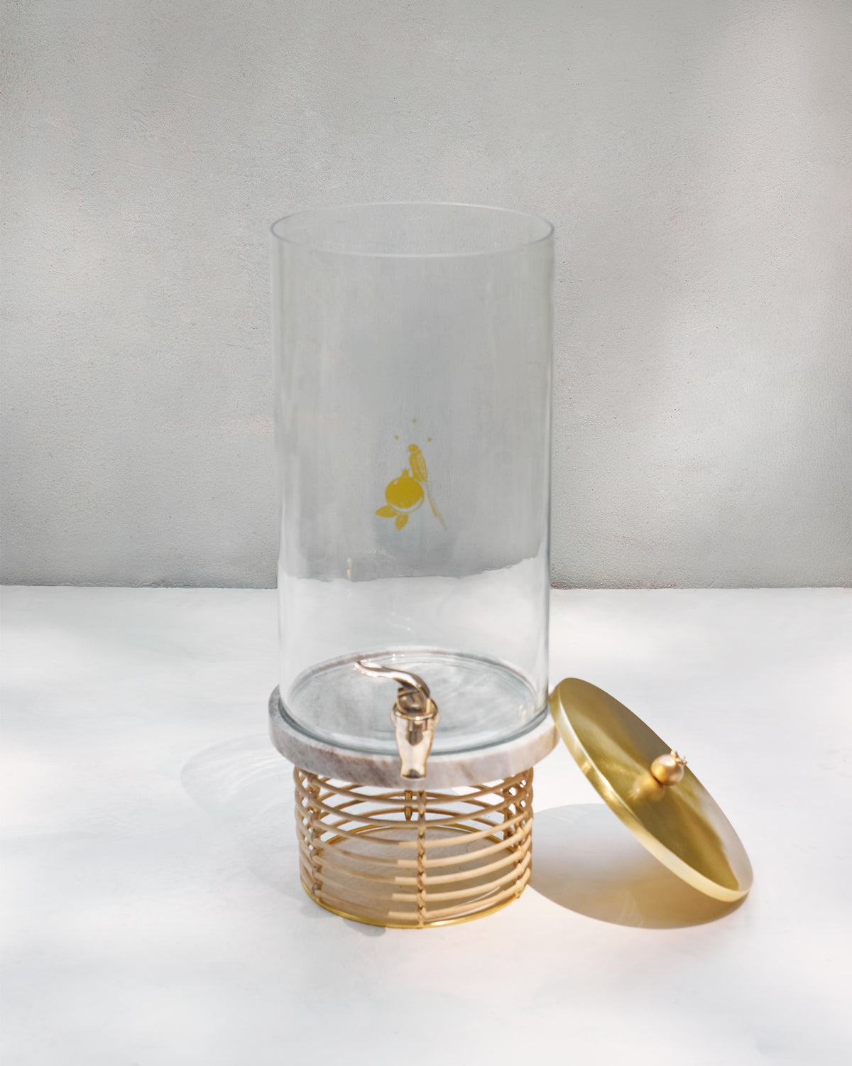 Mistle glass dispenser with gold tap, marble base, and lid beside the stand.