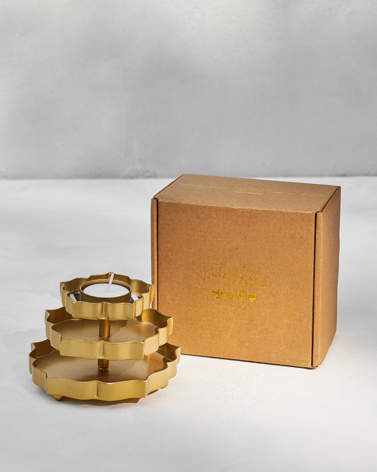 Gold Sama votive shown beside a Nicobar kraft gift box.