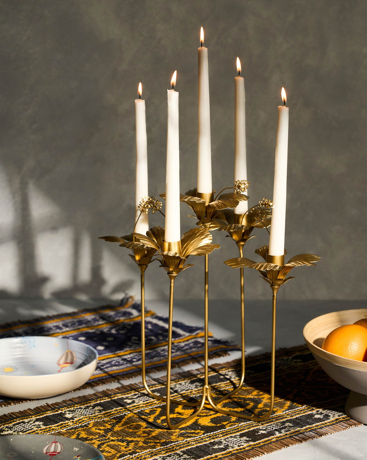 Gold hibiscus candle holder with lit tapers on a table.