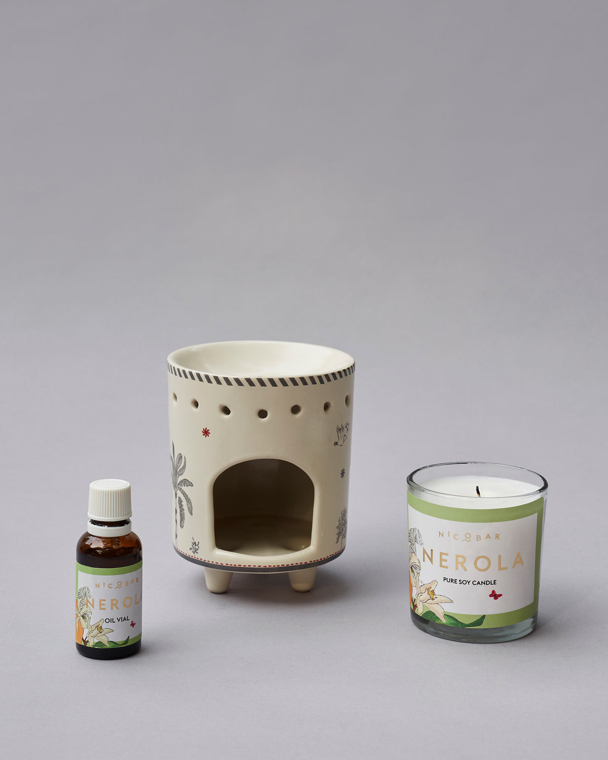 Ceramic burner with an arched opening, beside an oil vial and soy candle.