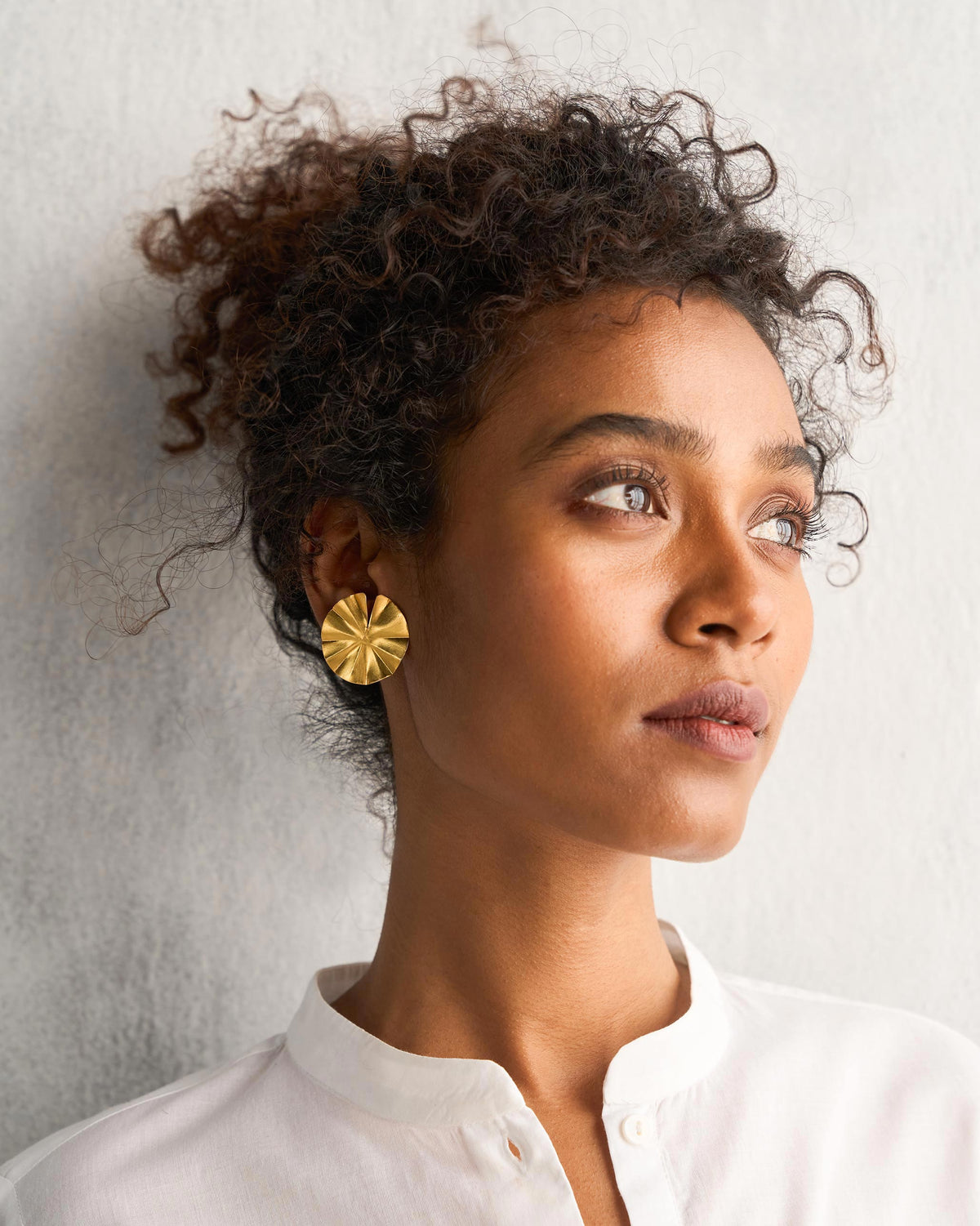 Person wearing Small Lilly Pad Stud, a round gold stud with ridged petals.