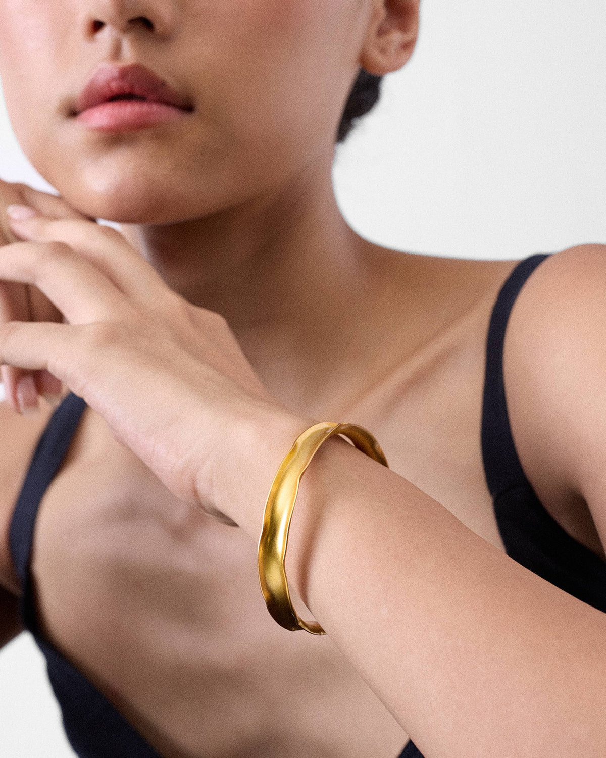 Close-up of a thin gold Batur bangle with a wavy cuff shape on a wrist.