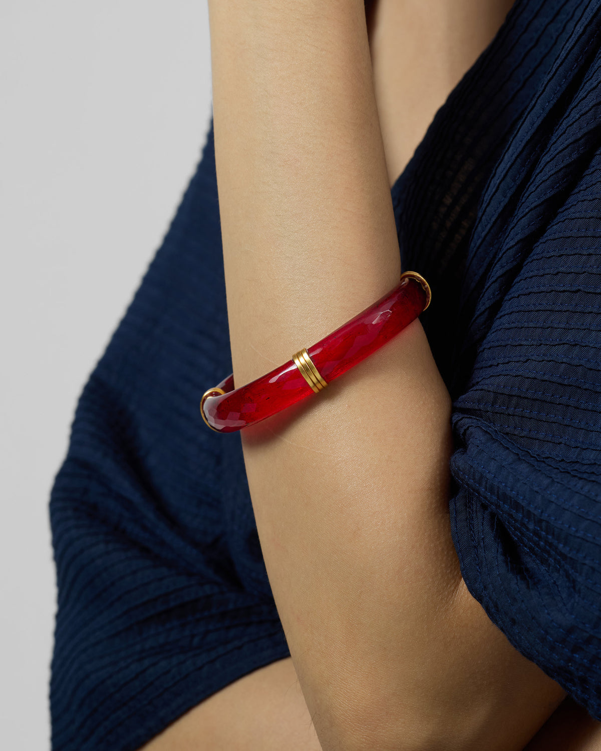 Translucent red glass bangle with gold ribbed bands worn on a wrist.