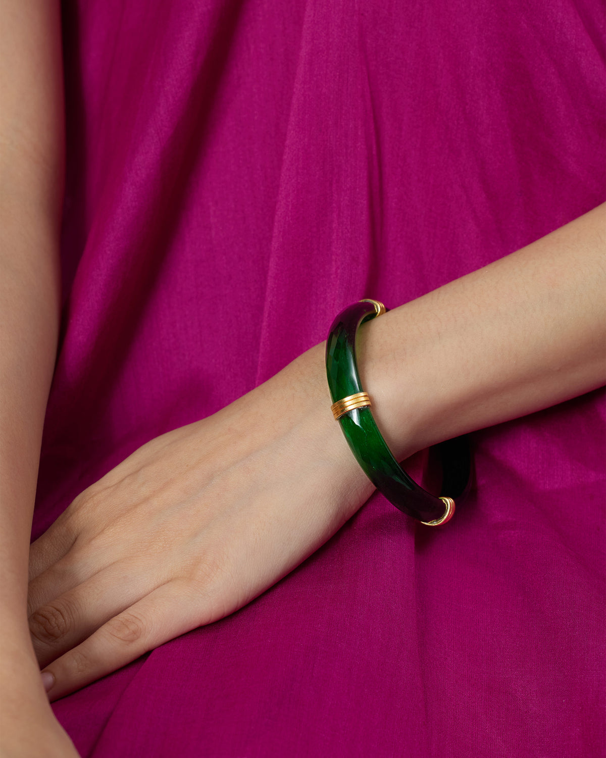 Green Cara glass bangle with gold spacers worn on a wrist.