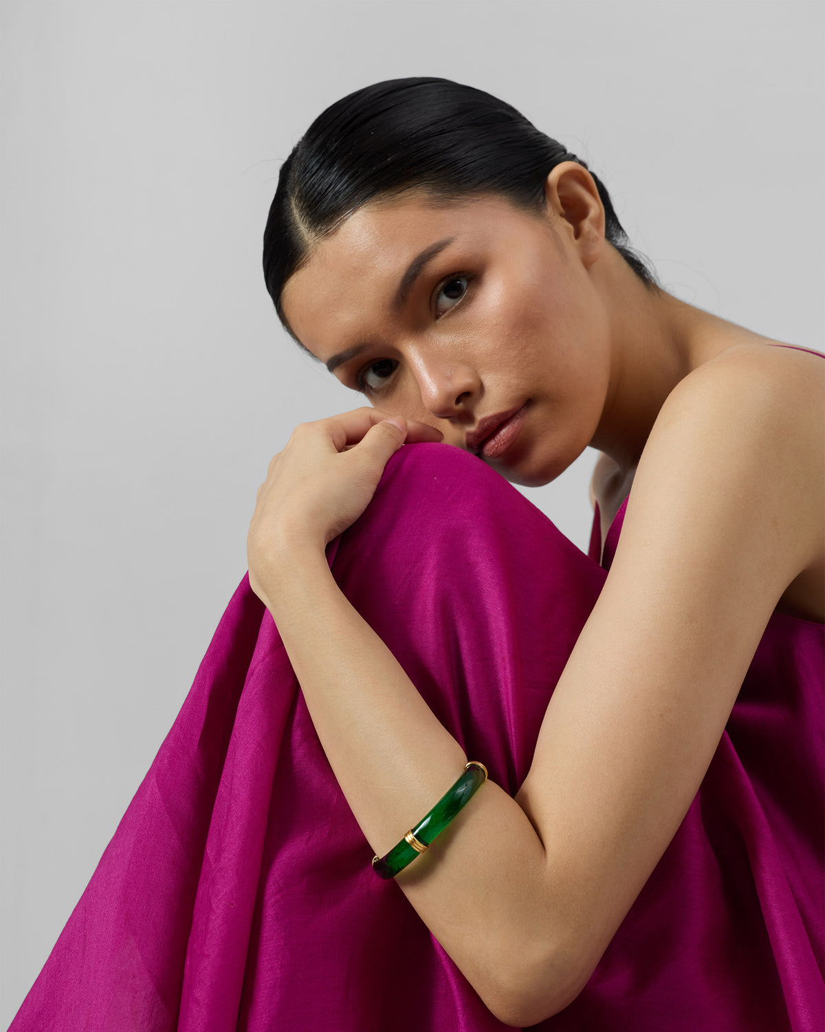 Person wearing a green Cara glass bangle with gold spacers.
