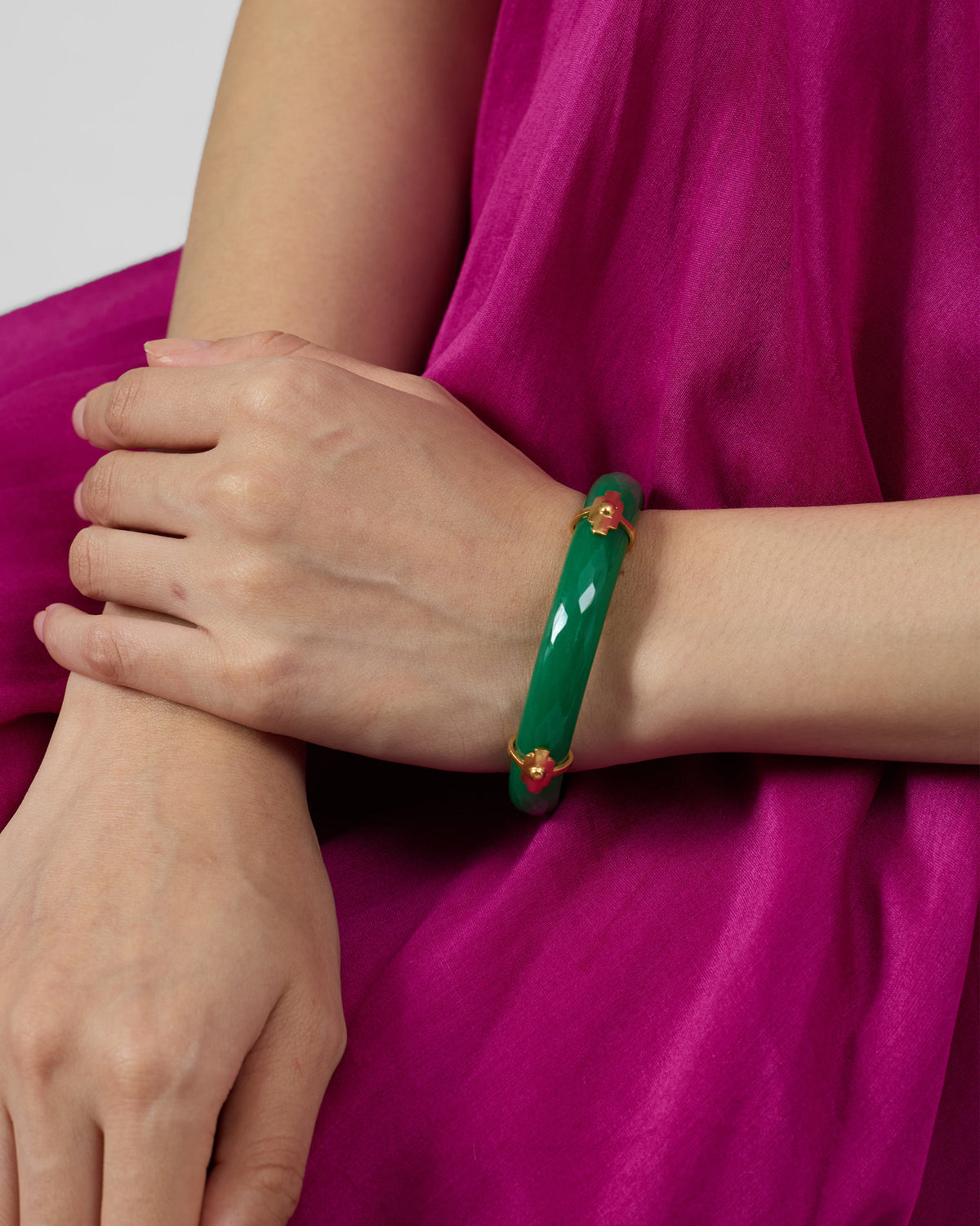 Glossy green glass bangle with gold floral accents worn on a wrist.