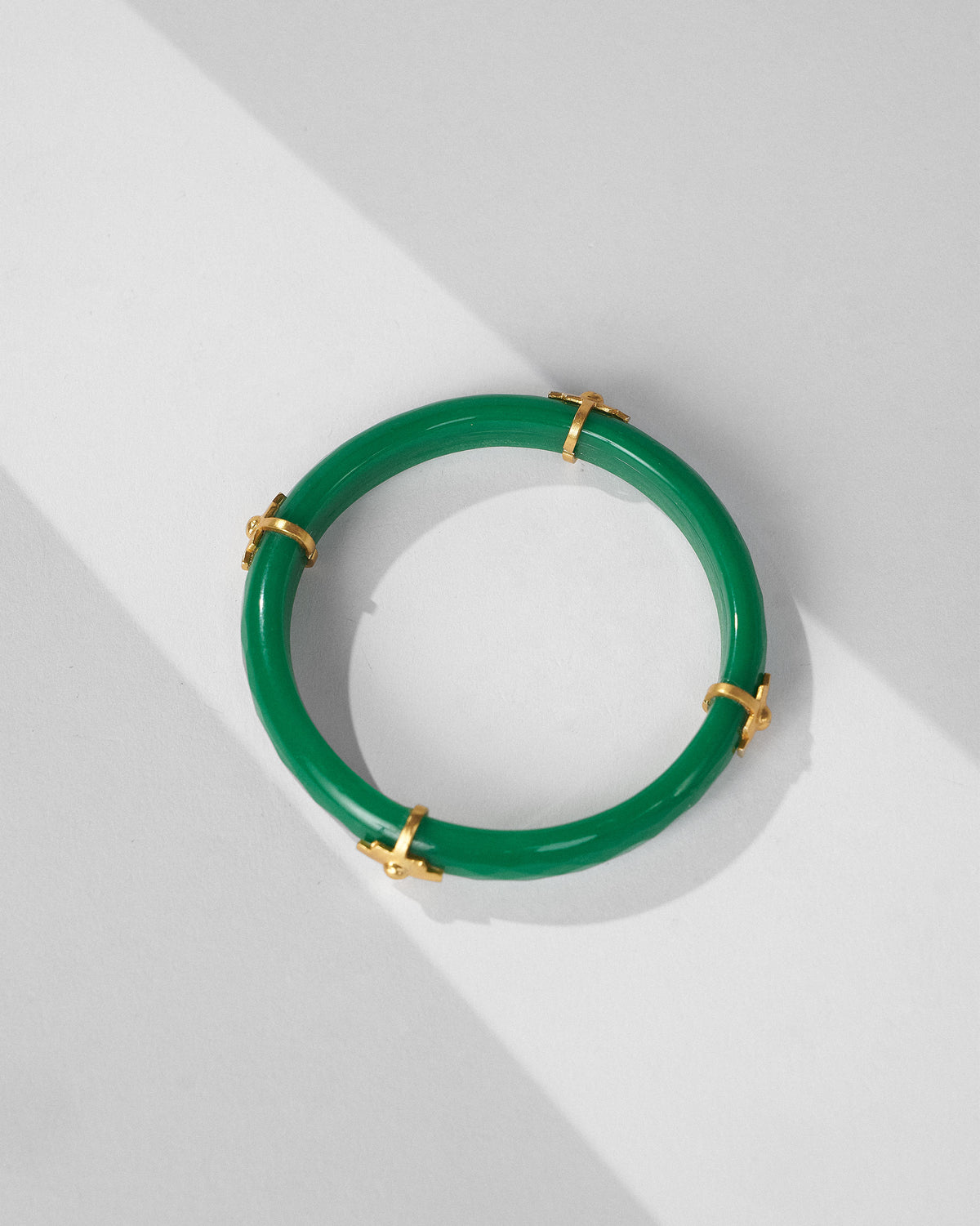 Overhead view of a green glass bangle with four gold cross accents.