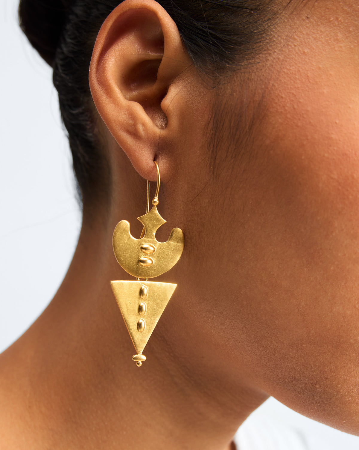 Person wearing gold Lama Earrings with a triangular drop.