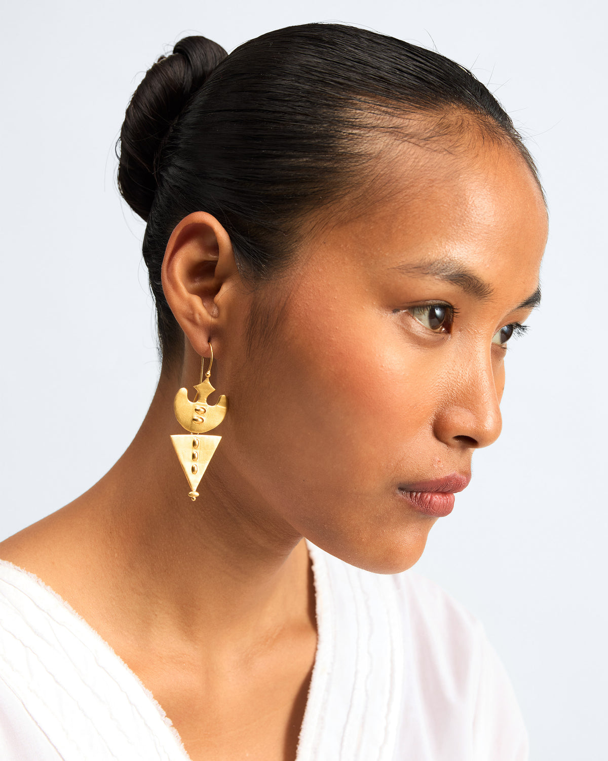 Side view of gold Lama Earrings worn on a person.