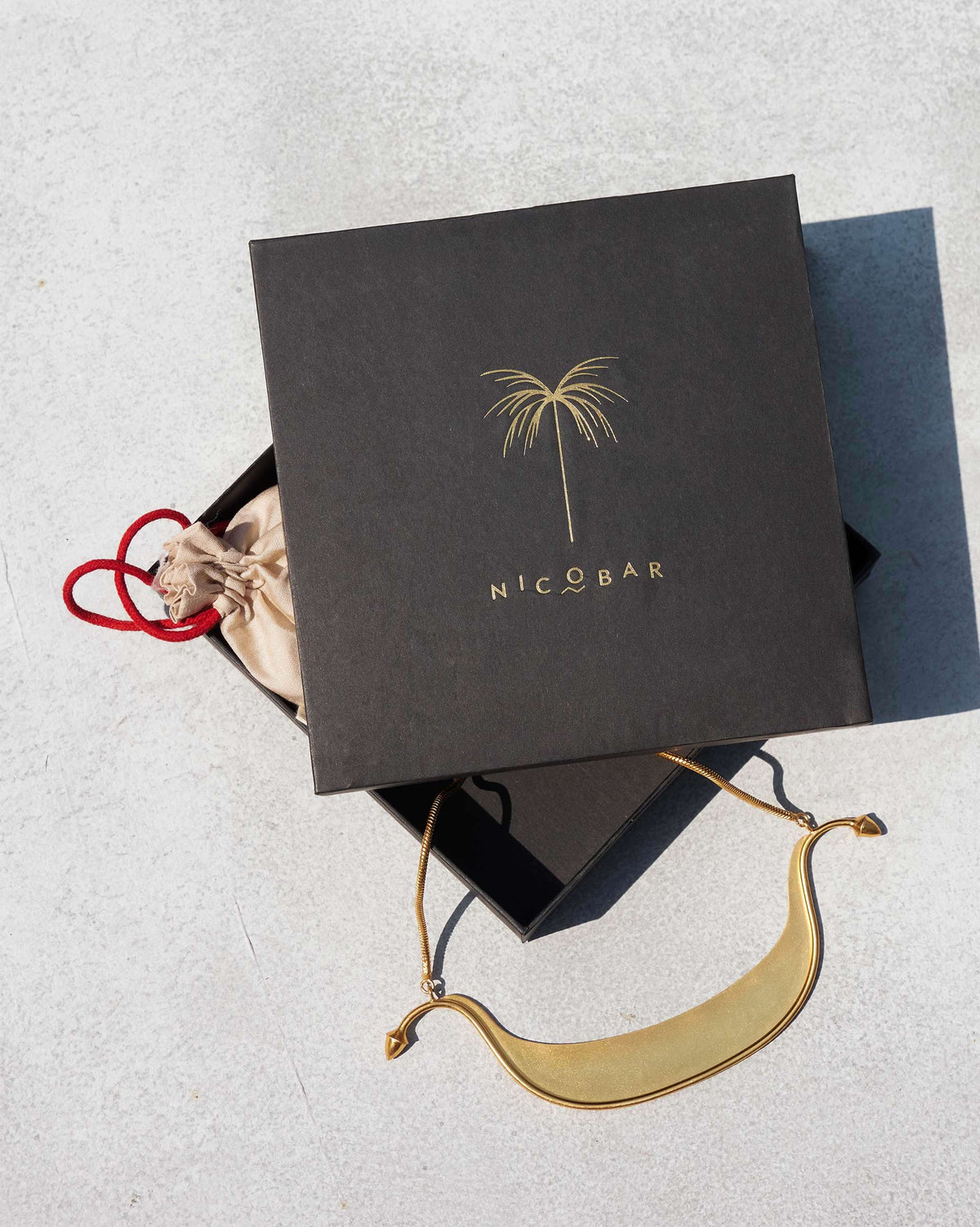 Gold Musafir Necklace lying beside a black gift box and cream pouch.