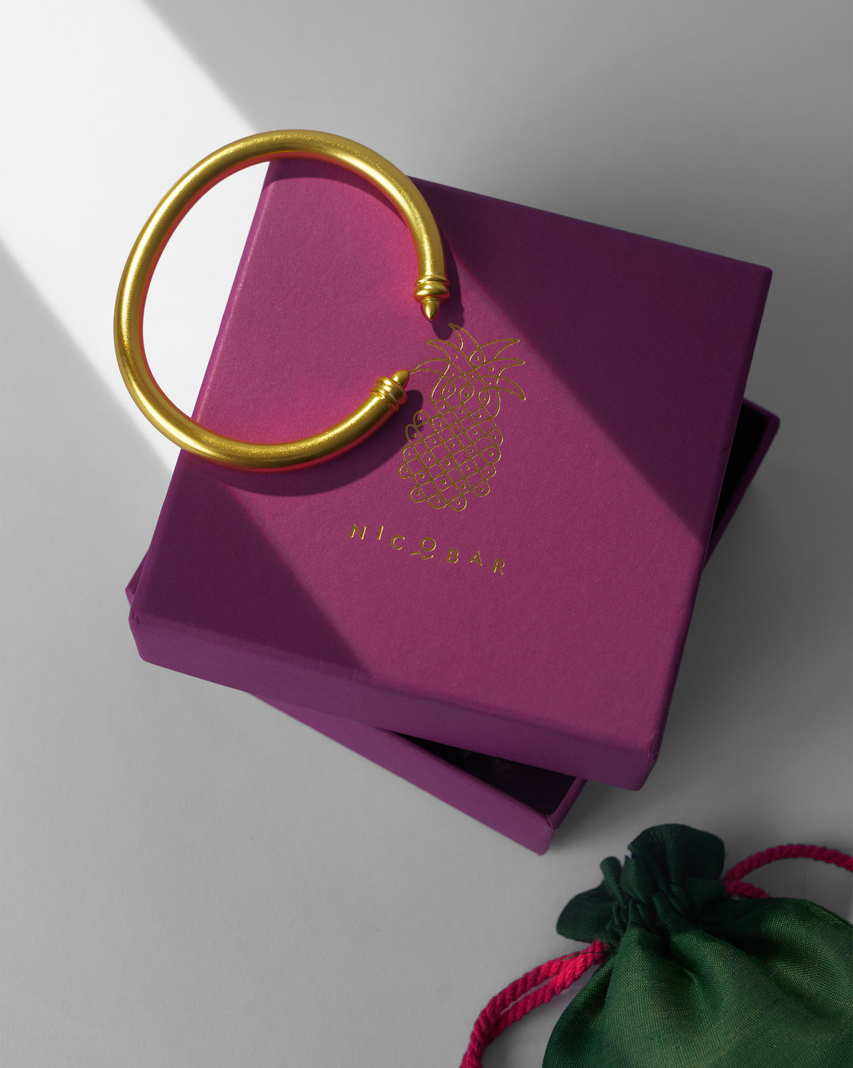 Gold Raahi open cuff bangle on a purple Nicobar gift box.