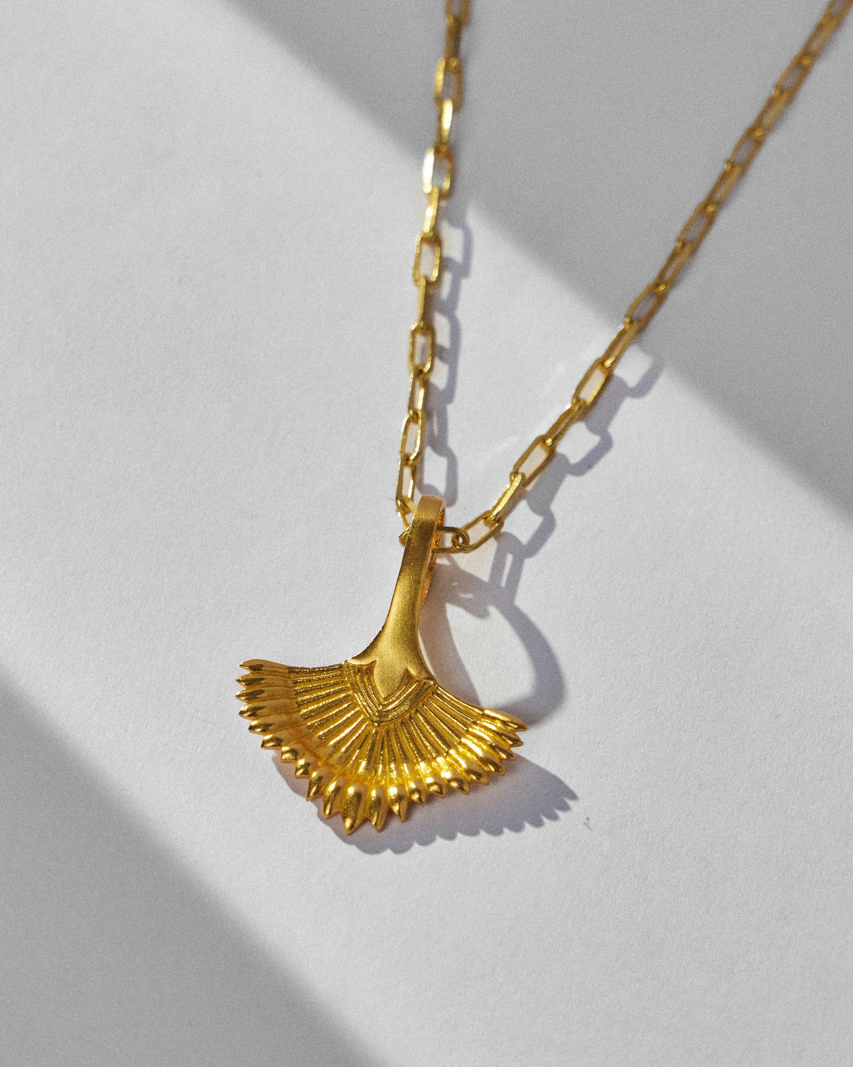 Close-up of a gold palm necklace pendant showing scalloped leaf tips.