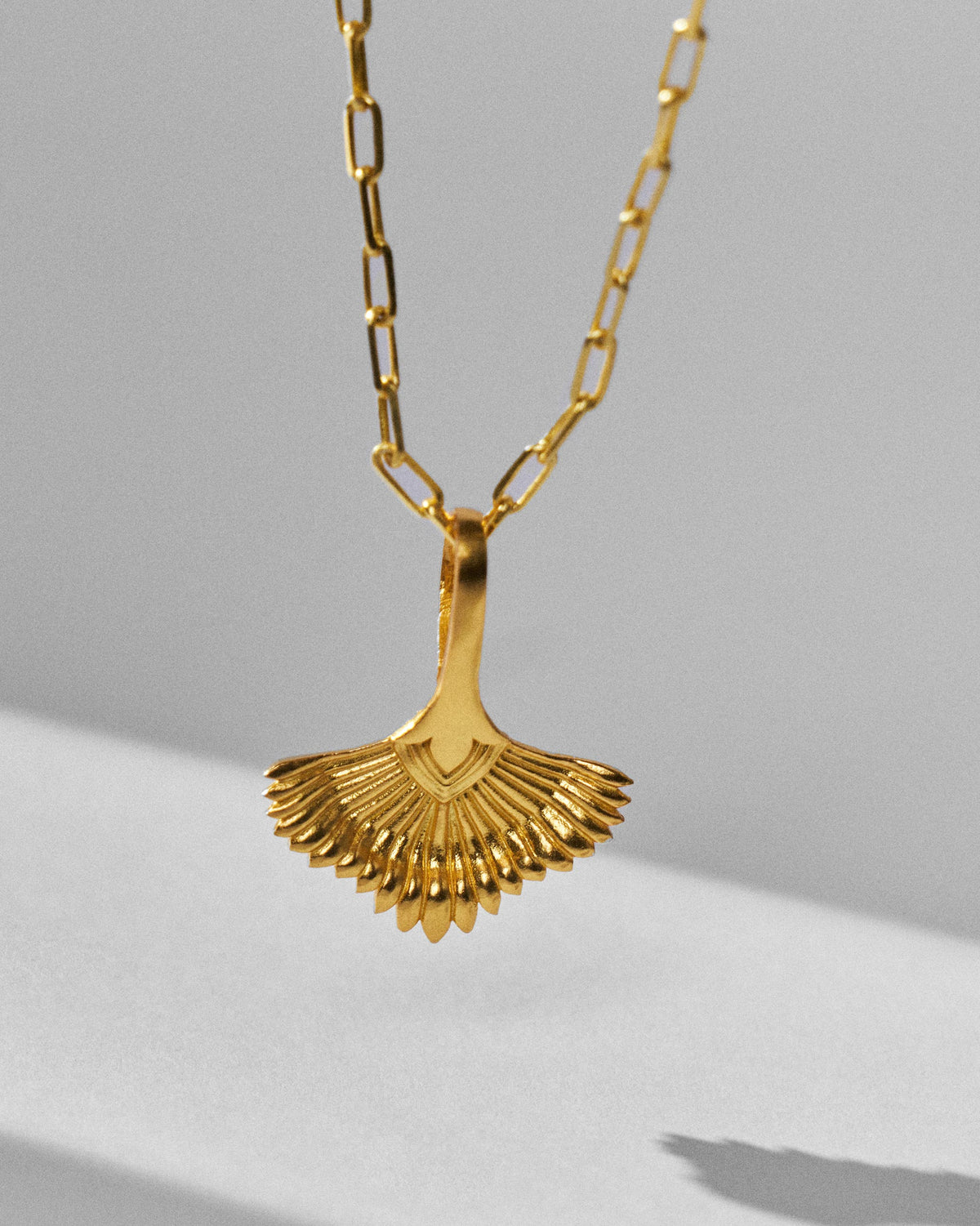 Close-up of a gold palm necklace pendant with ribbed leaf texture.