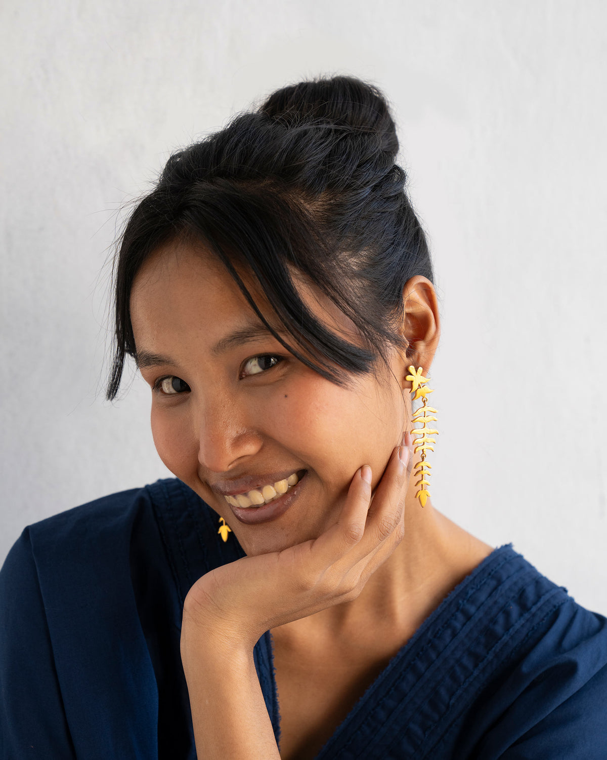Person wearing long gold Myra Earrings with a stacked leaf design.