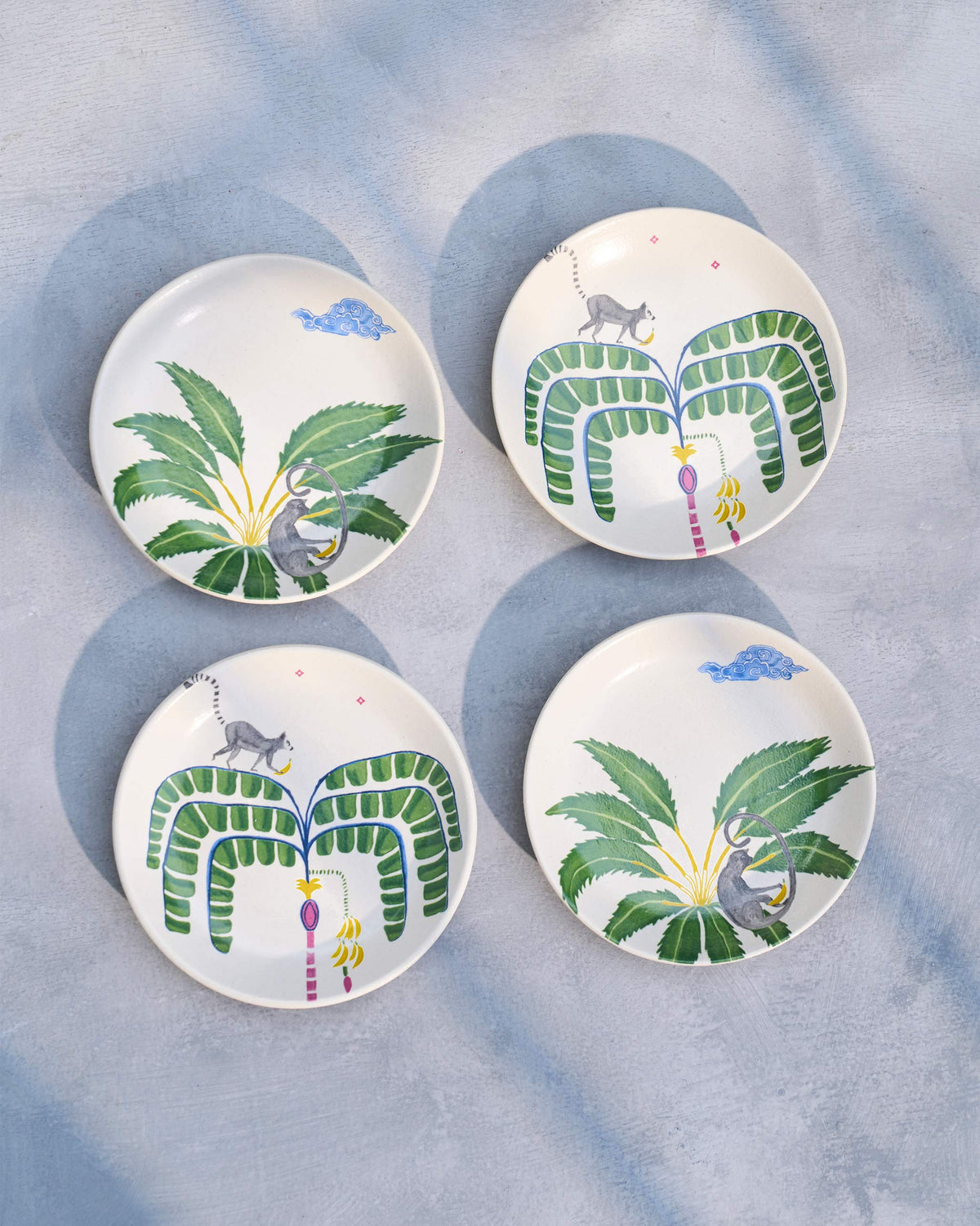 Four Safari tea plates with a painted palm and grey animal motif.