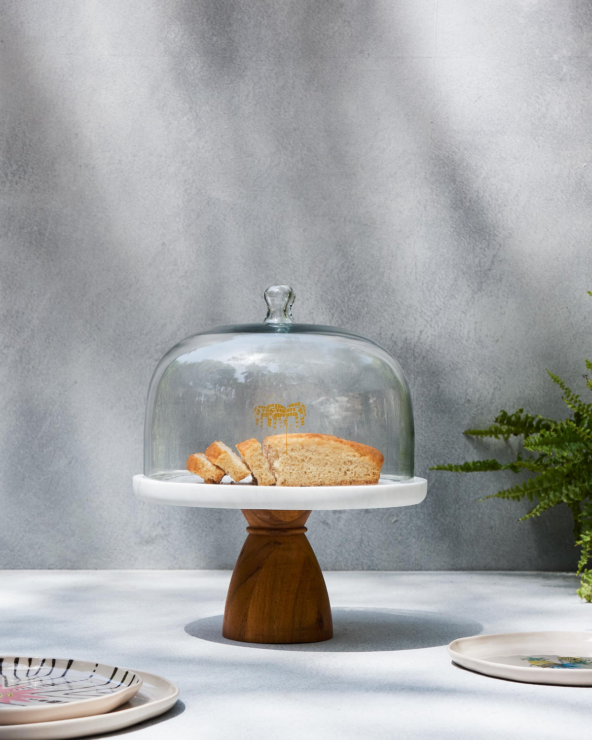 Safari Cloche with a glass dome on a marble stand and wooden pedestal.