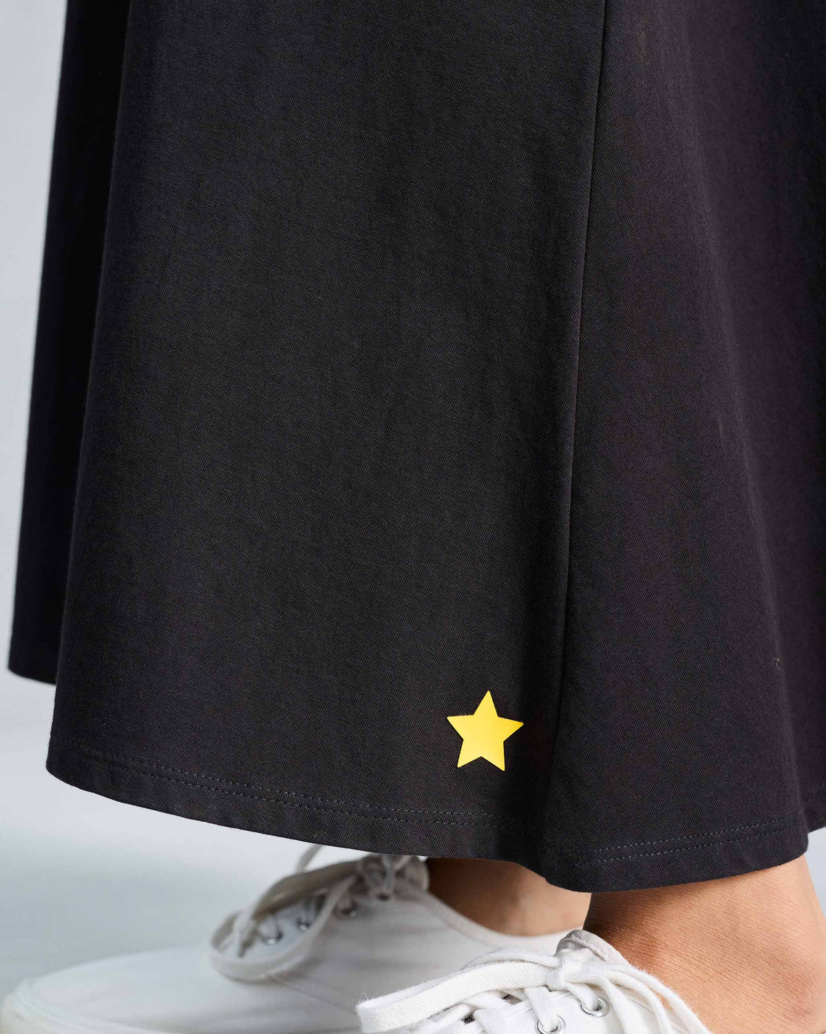 Close-up of a yellow star near the hem of a black Esther dress.