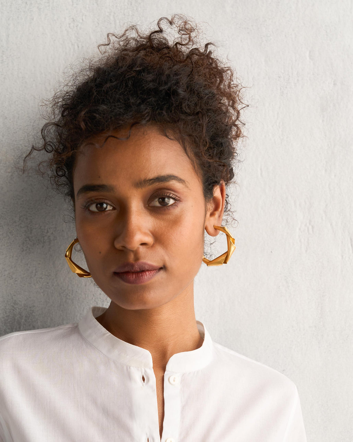 Person wearing Ribbon Hoop Small gold earrings.