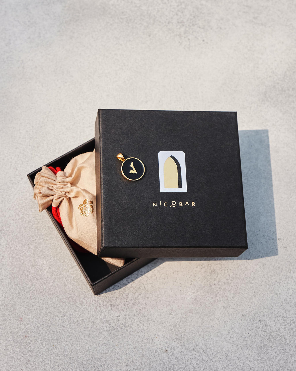 Alphabet C charm on a black Nicobar gift box with a cream pouch.
