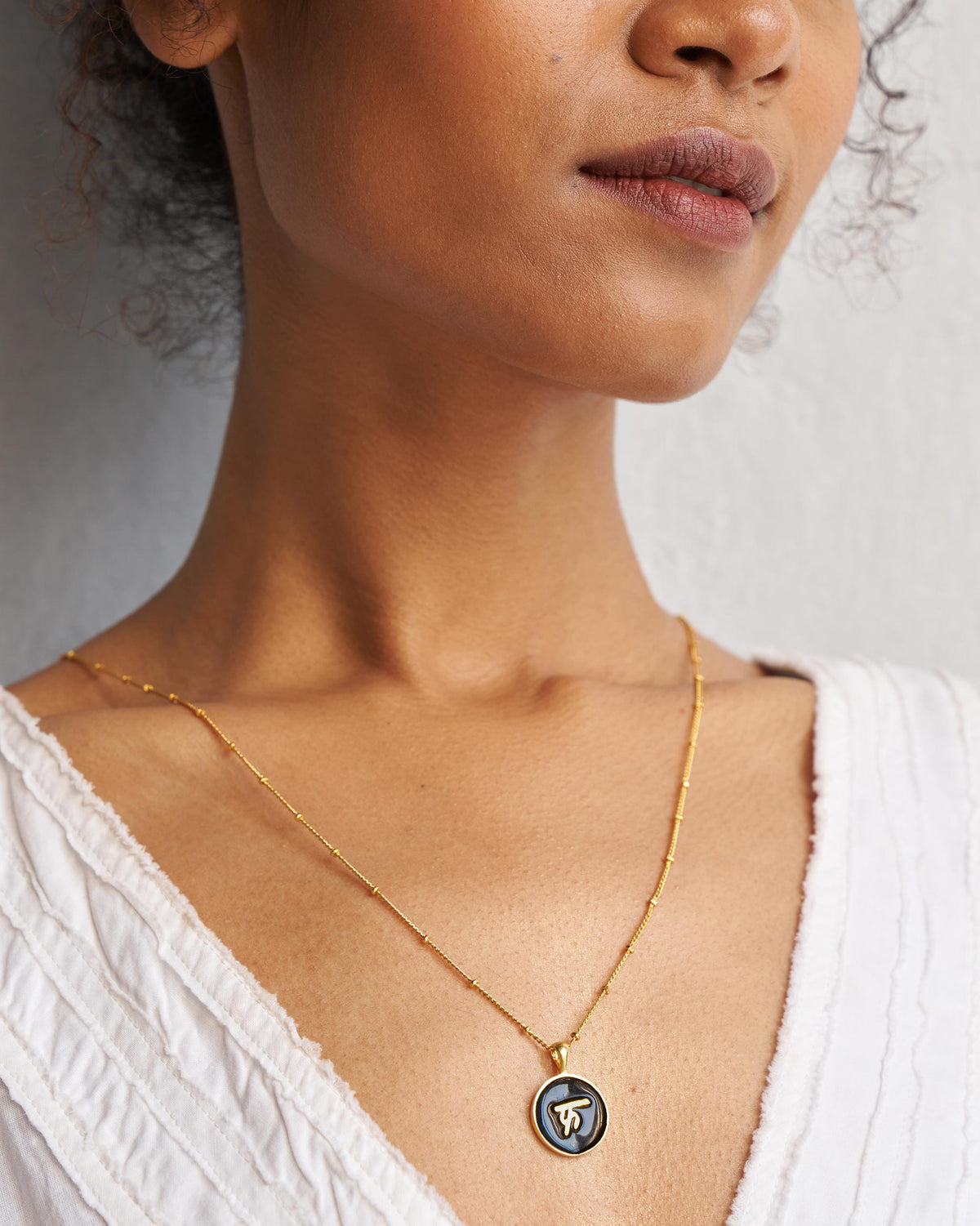 Alphabet F charm in black and gold worn on a fine gold chain.