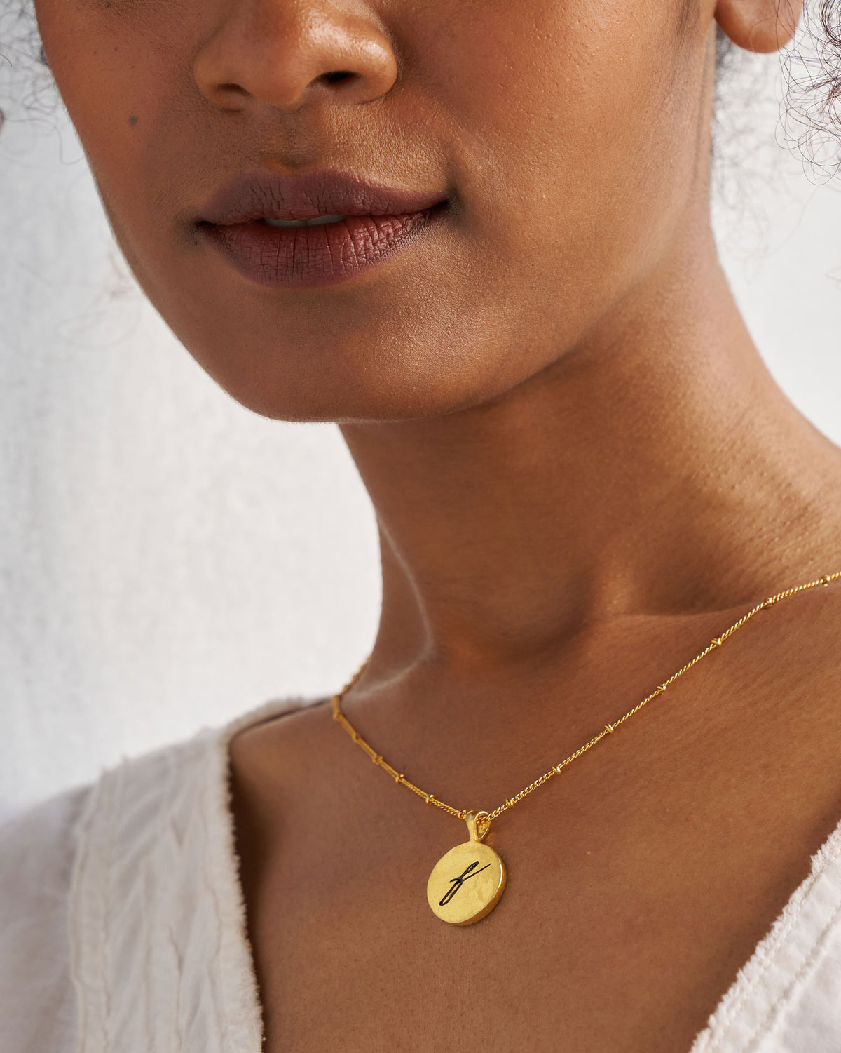Alphabet F charm with a black script f worn on a gold chain.