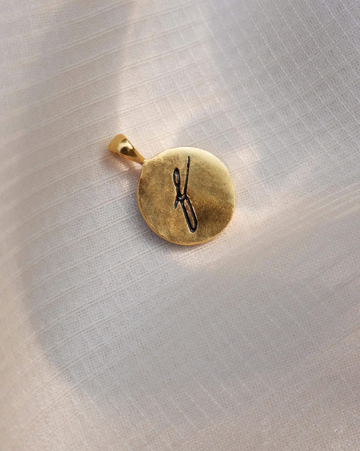 Close-up of a gold alphabet charm with a black script letter.