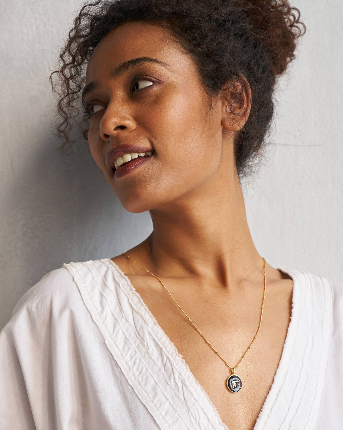 Alphabet F charm worn on a gold chain with a white V-neck top.