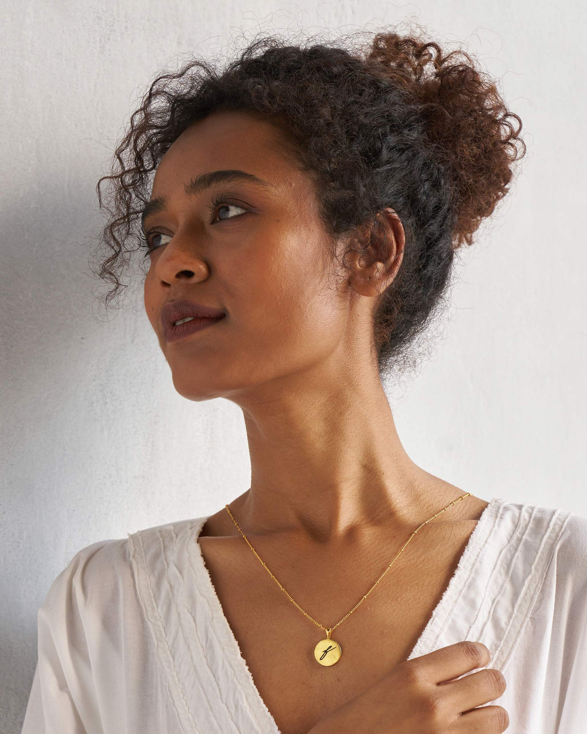Alphabet F charm necklace worn with a white V-neck top.
