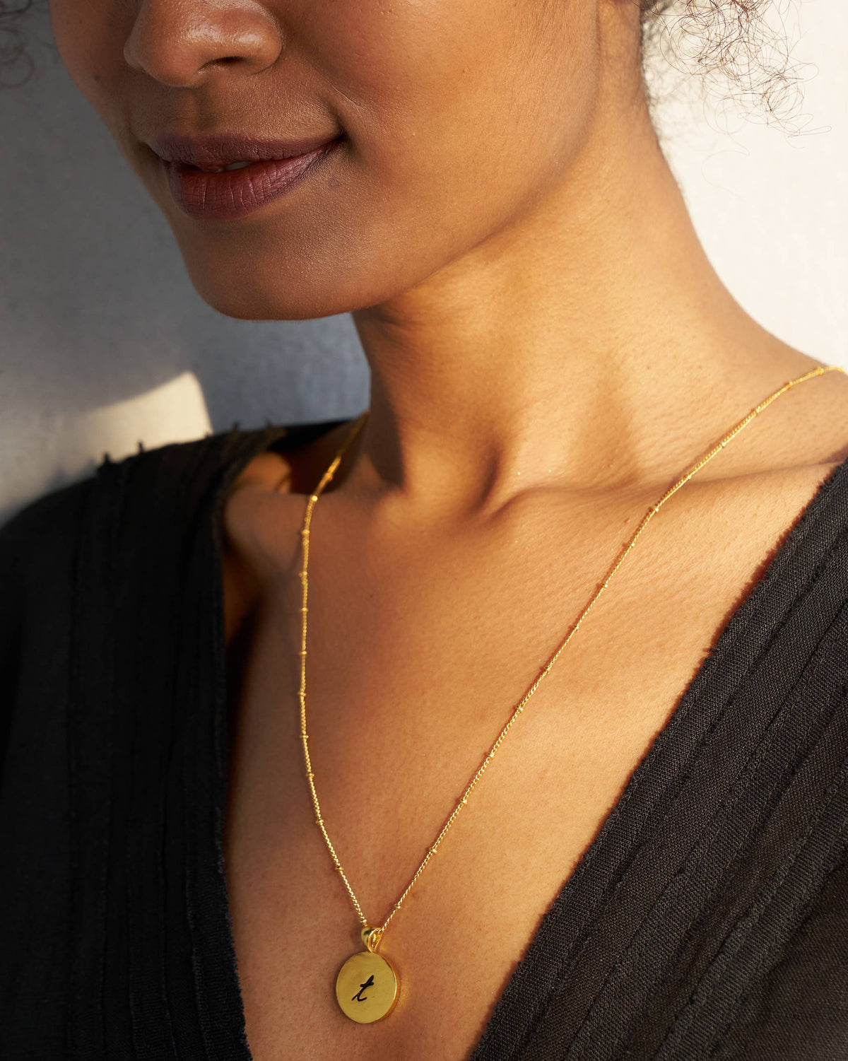 Alphabet T charm with a black letter t on gold, worn on a satellite chain.