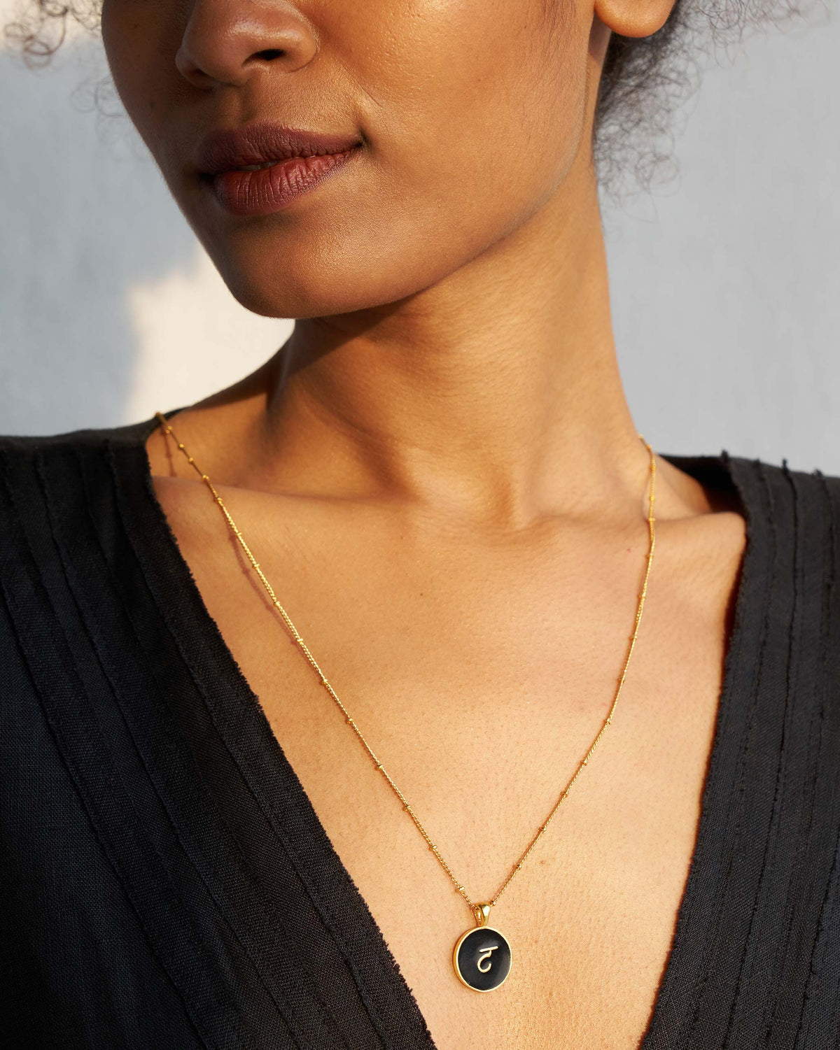 Alphabet T charm showing gold Devanagari letter on black enamel, worn on a chain.