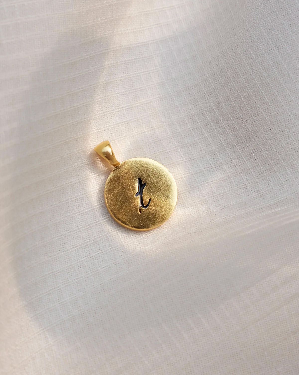 Close-up of Alphabet T charm with a black letter t on a gold disc.