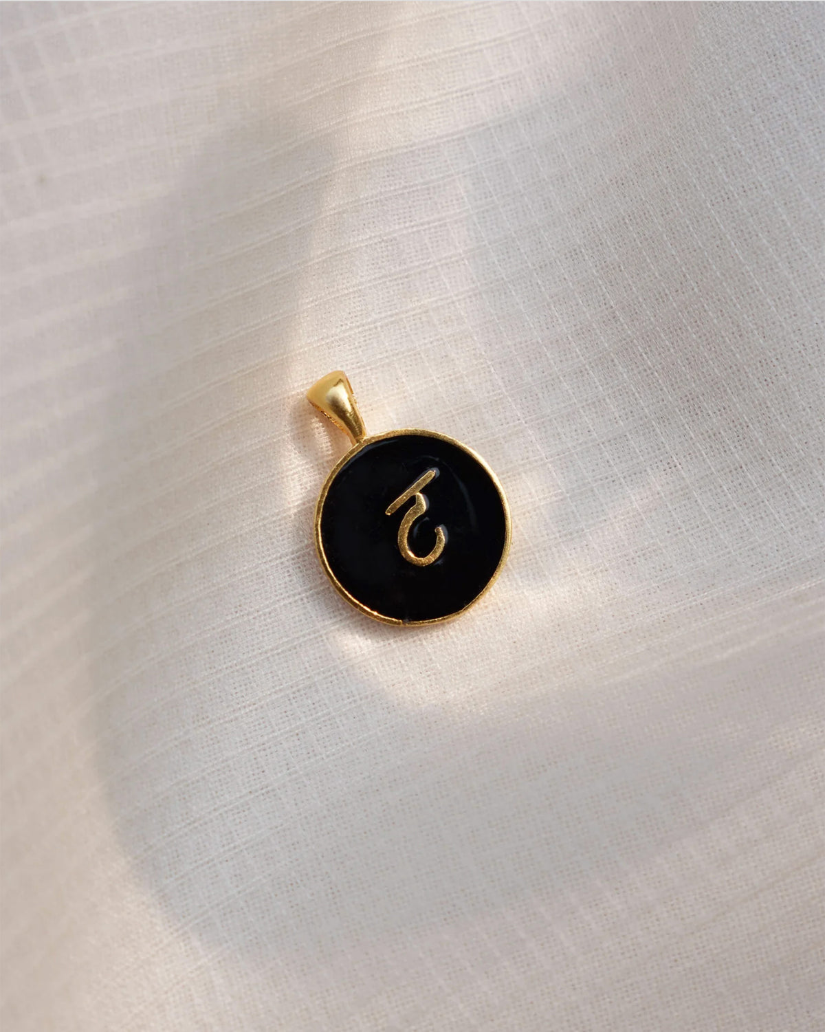 Close-up of Alphabet T charm with gold Devanagari letter on black enamel.