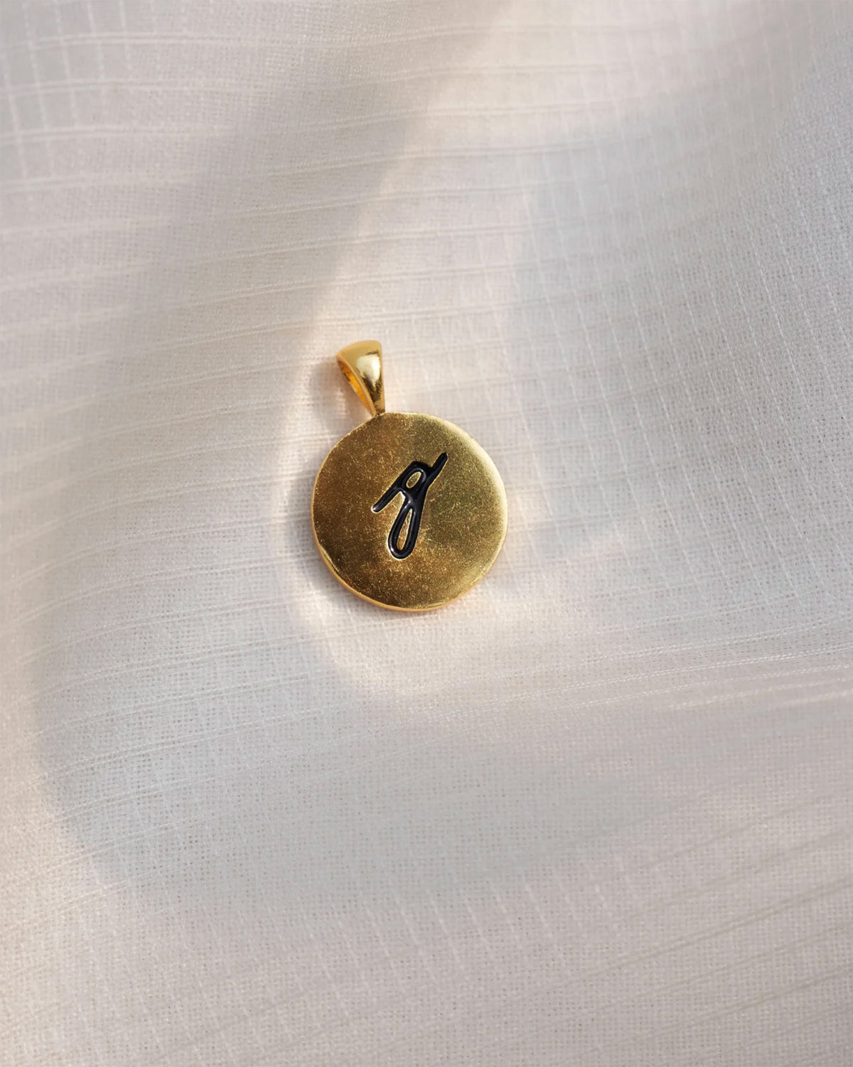 Close-up of a gold Alphabet G charm with a black script g.
