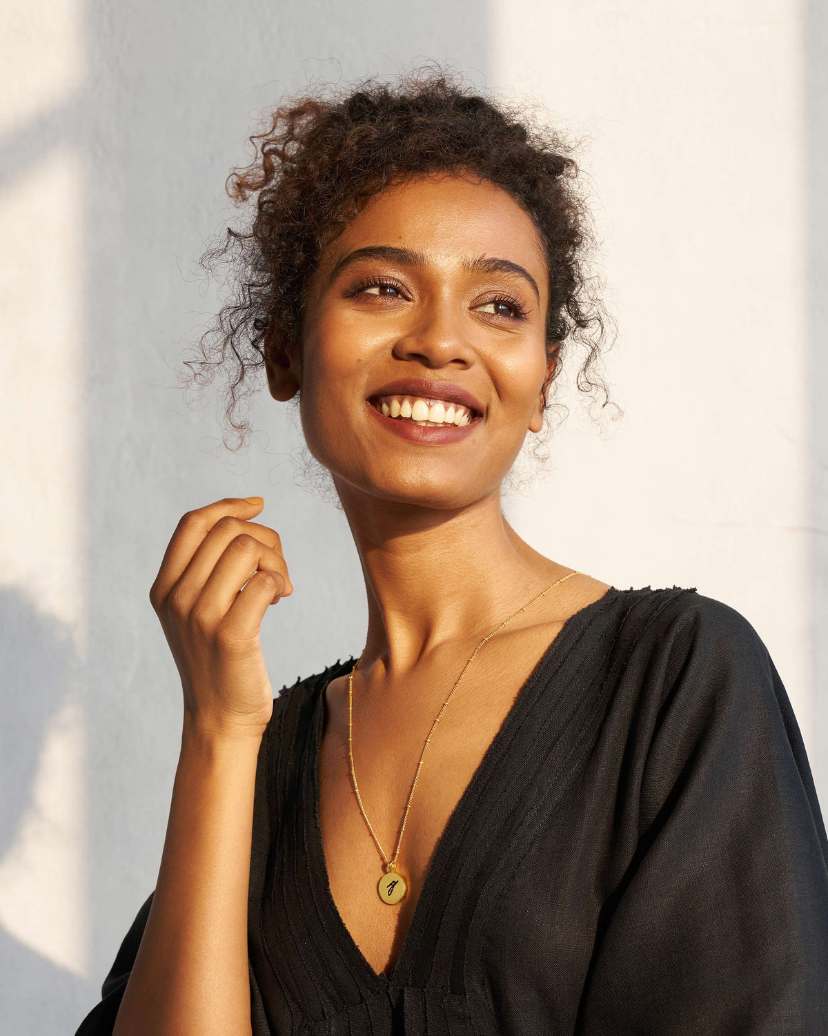 Person wearing a black and gold alphabet charm necklace.