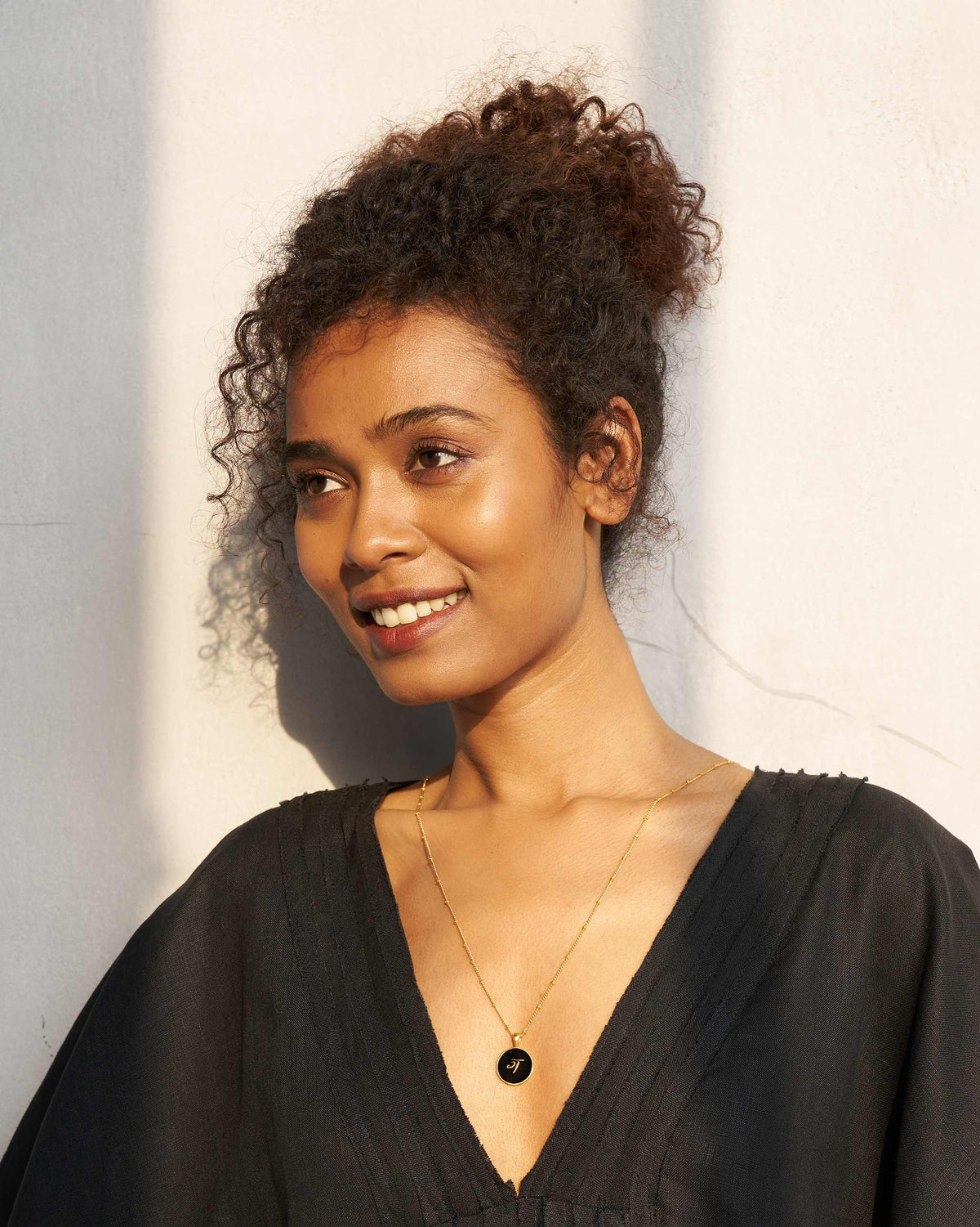 Person wearing a black and gold alphabet charm necklace.