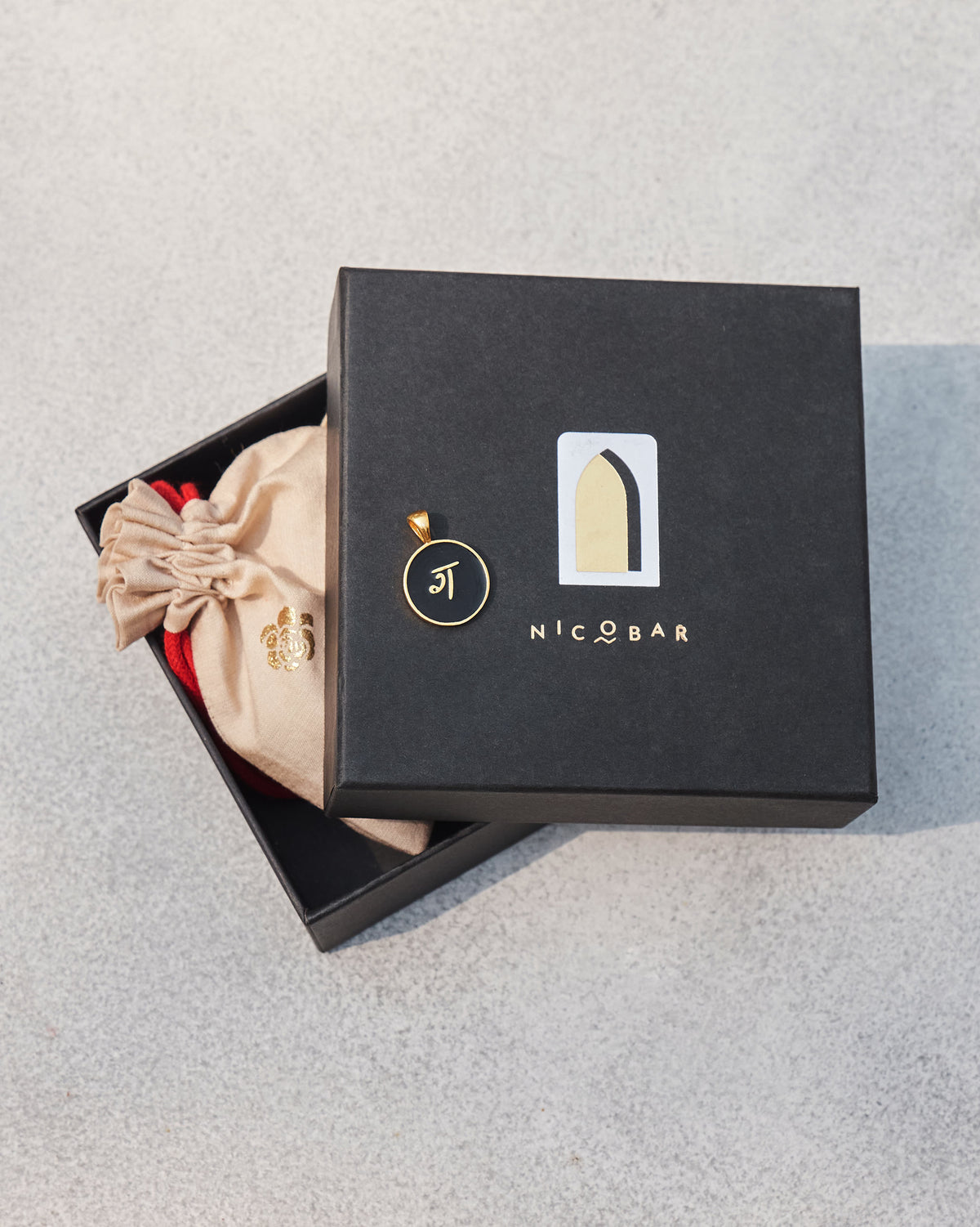 Alphabet G charm in black and gold on a Nicobar gift box.