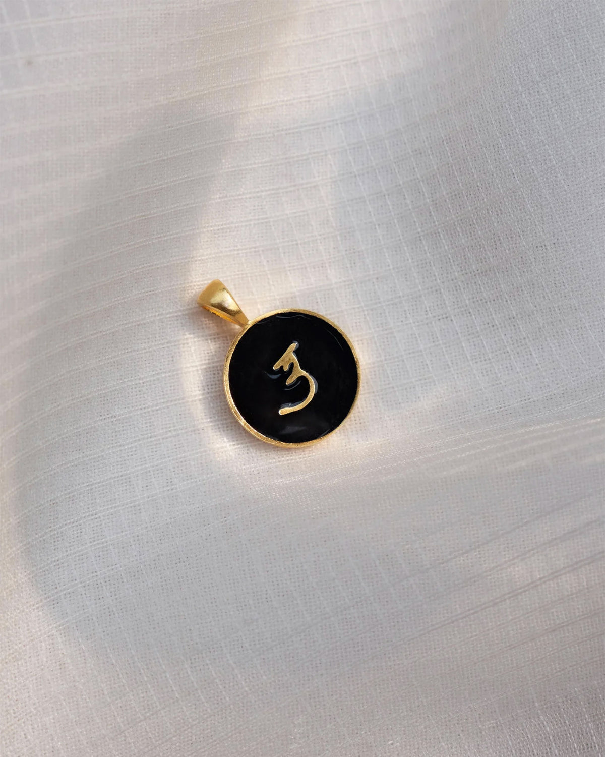 Close-up of a black and gold Alphabet U charm showing a Devanagari letter.