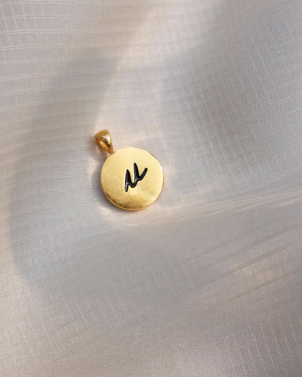 Close-up of a gold Alphabet U charm with a black script u.