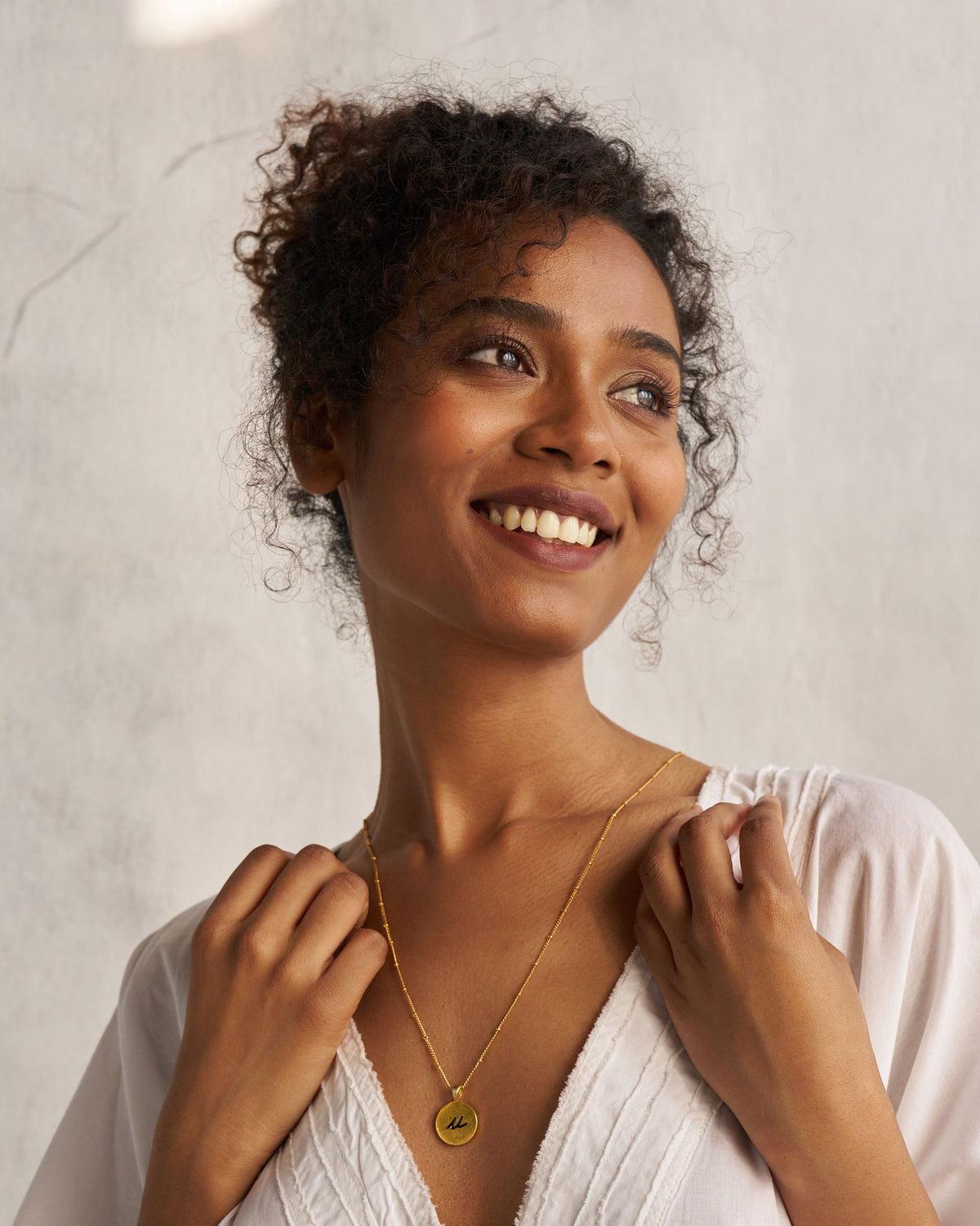 Person wearing a gold Alphabet U charm on a fine chain.