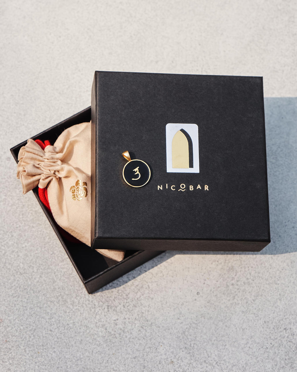 Black and gold Alphabet U charm on a Nicobar gift box.