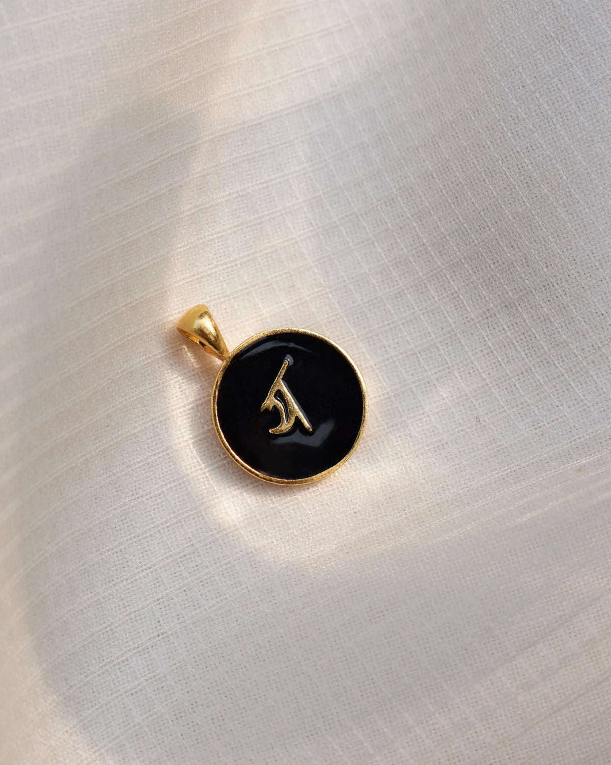 Close-up of a black and gold Alphabet Y charm showing a Devanagari letter.