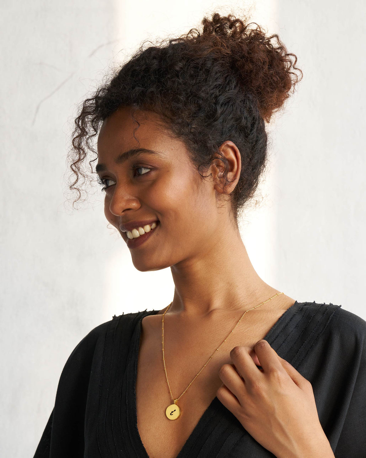 Person wearing a gold Alphabet I charm on a fine chain.