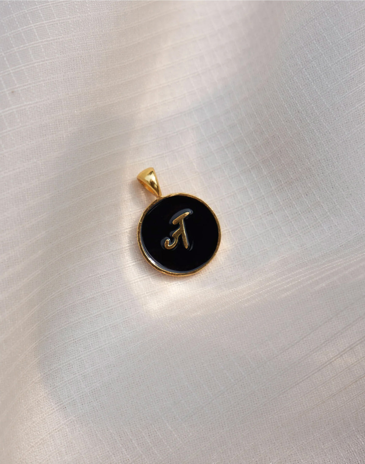 Close-up of a black and gold Alphabet J charm showing a Devanagari letter.