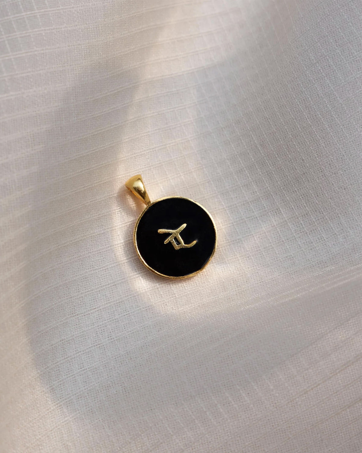 Close-up of a black enamel alphabet charm with a raised gold letter.