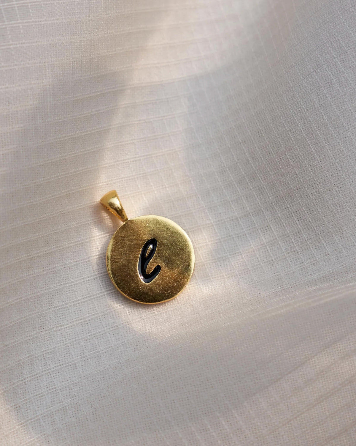 Close-up of a gold alphabet charm with a black script letter.