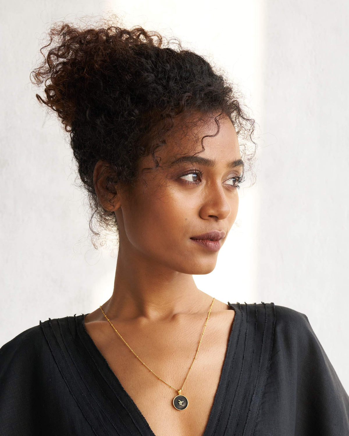 Person wearing a black and gold alphabet charm necklace.