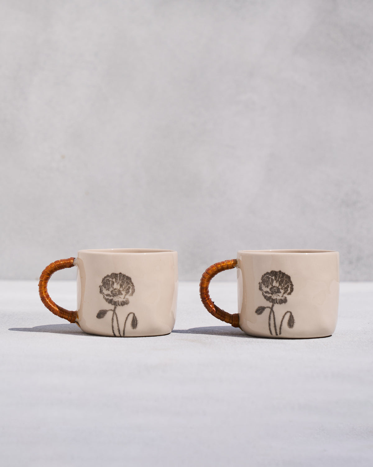 Set of two Poppy mugs with rattan handles and black poppy prints.